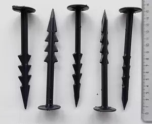 The image shows five black landscape fabric stakes with sharp points for securing fabric, alongside a ruler.