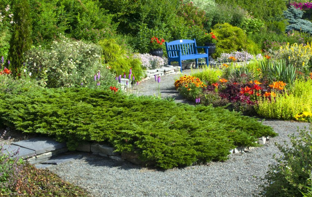 A garden setting featuring green granite gravel around plants and a blue bench with a pathway leading through the garden