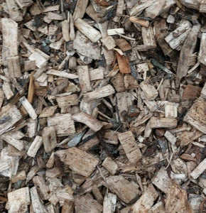 A close-up of wood mulch, consisting of small, uneven pieces of wood chips in light brown and beige colors.