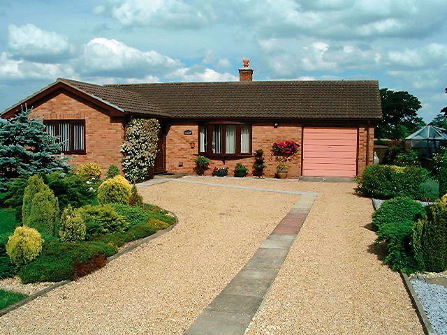 A residential garden with a pathway leading to a house, featuring a mix of greenery and golden gravel.