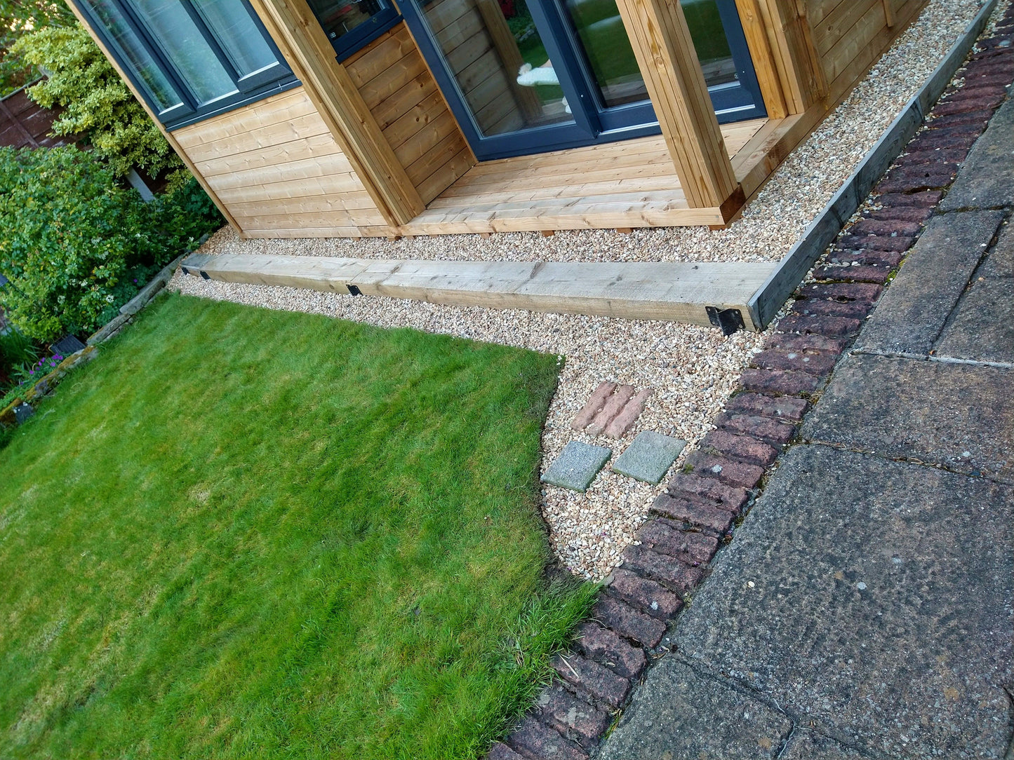 A garden with a pathway lined with golden gravel, leading to a wooden door and a brick wall on one side.