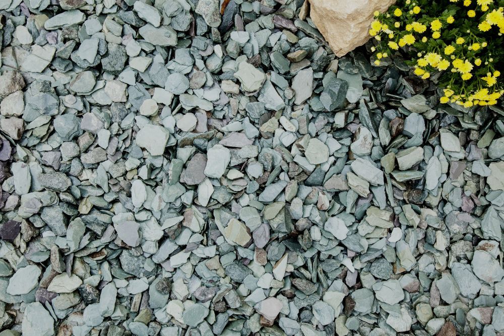 A close-up image of green slate chippings, featuring a mix of various shades of green and some gray, laid on a surface.