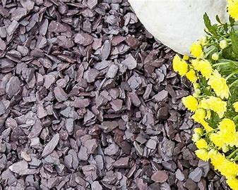 Purple slate chippings used as garden mulch beside yellow flowers.